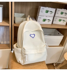 Detail shot of a cream student backpack with purple heart embroidery on a wooden shelf