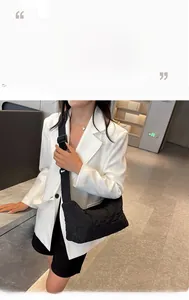 Detail view of the black quilted nylon tote bag worn by a model in white blazer