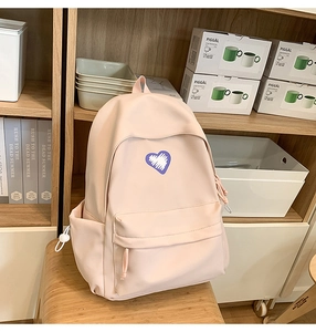 Detail of light pink backpack with heart patch showing front pocket and side bottle holder
