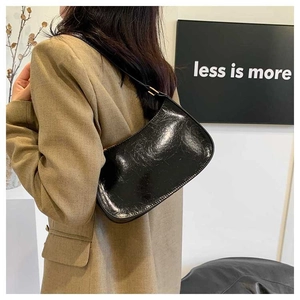 Polished black leather baguette shoulder bag with wrinkled texture worn by model