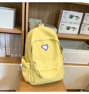 Macro detail of yellow student backpack with heart graphic on a wooden chair