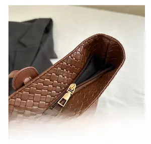 Detail of smooth gold metal zipper and brown woven leather texture on a tote bag