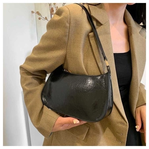 Close-up of a black glossy leather baguette bag with elegant golden metal buckles