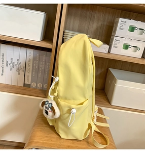 Detail view of yellow nylon backpack side pocket with white drawstring and dog plush charm