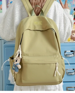 Close-up of olive green nylon backpack with yellow embroidery and cute bear pendant