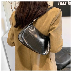 Detail of minimalist black glossy leather shoulder bag with textured surface on model