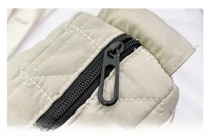 Close-up of beige quilted tote bag showing black resin zipper and white stitching detail