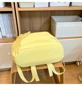 Detail of a lemon yellow nylon backpack on a wooden bench with multiple zip pockets