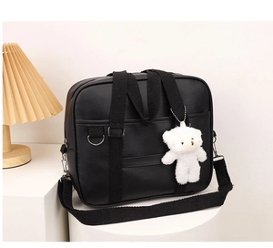 Detail of JK style black PU leather handbag featuring a cute plush bear charm and strap