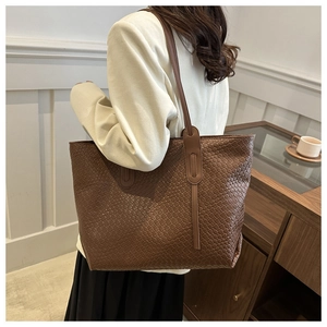 Detail of a dark brown woven leather tote bag shown on a model in a lifestyle setting