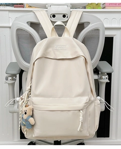 Close-up of beige minimalist backpack featuring XINFEIDA embroidery and a blue bear plush charm