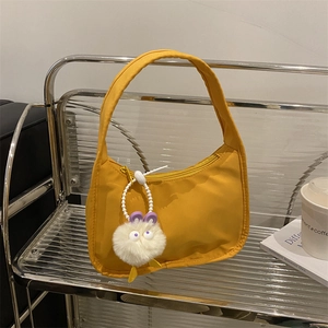 Chic yellow nylon hobo handbag with a plush charm displayed on a stylish urban shelf