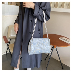 Détail du sac à bandoulière bleu clair avec jacquard papillon doré et bandoulière chaîne