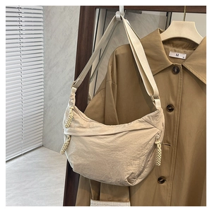 Détail d'un sac demi-lune beige en nylon avec pompon tressé sur un trench-coat marron