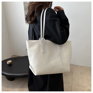 Detail of white woven texture tote bag with slim straps worn on a shoulder
