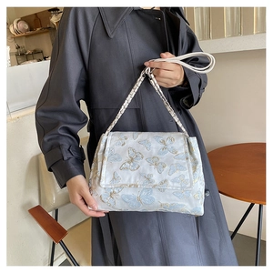 Détail des broderies papillons et de la bandoulière en chaîne sur un sac gris
