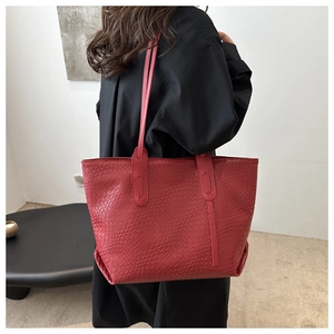 Detailed view of red woven shoulder bag with wide strap on model in modern interior
