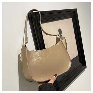 Detail of a beige glossy faux leather baguette bag with a sleek hobo design and metal zipper