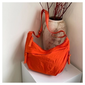 Détail d'un sac hobo demi-lune en nylon orange vif avec sangle large et tirette de zip nouée