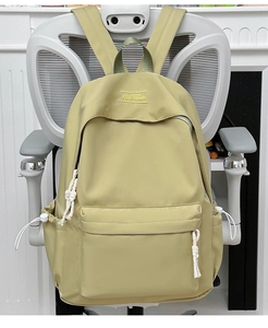 Close-up of a pastel yellow nylon backpack with embroidered brand logo and white woven zip cord