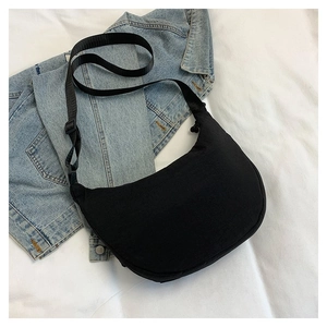 Détail d'un sac bandoulière demi-lune noir sur tissu blanc avec veste en jean