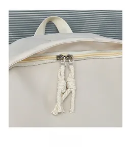Detail of smooth metal double zippers with woven rope knots on a cream white backpack
