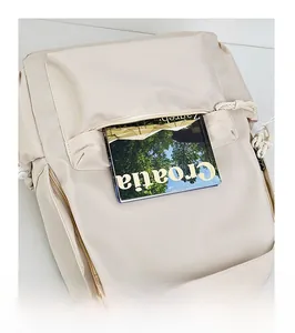 Close-up of front zipper pocket on beige nylon backpack showing storage capacity for books