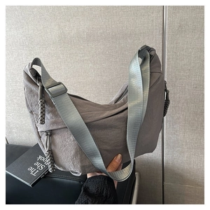 Gros plan d'un sac demi-lune en nylon gris avec bandoulière réglable et tirettes tressées