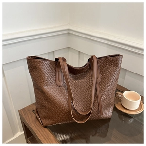 Detail shot of the woven texture and slim dual shoulder straps on a brown tote bag