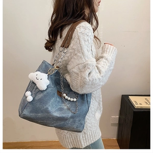 Détail du sac seau en toile bleu-gris avec bandoulière cuir chaîne et charme peluche