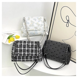 Détail de trois sacs bandoulière brodés avec chaînes sur un présentoir de style minimaliste