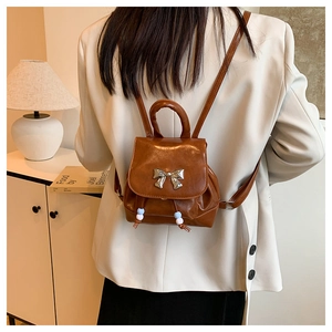 Detail of caramel brown glossy leather mini backpack with silver bow and drawstring