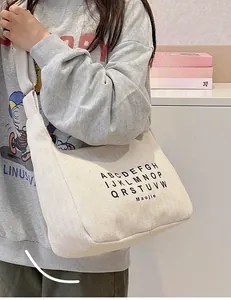 Detail view of the beige canvas crescent bag showing letter prints and wide shoulder strap