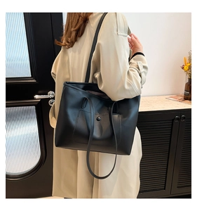 Detail of minimalist black matte leather tote bag featuring functional snap pocket and long straps