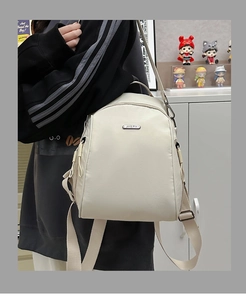 Detail of cream-colored versatile backpack showing metallic logo and nylon texture