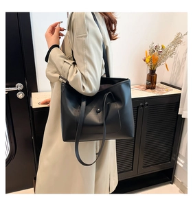 Detail shot of a large black leather tote bag worn by a model in a minimalist room