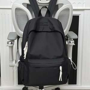 Black minimalist nylon backpack with white cord zipper pulls on an office chair