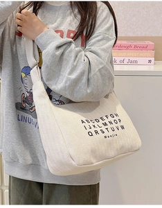 Beige corduroy hobo bag featuring black alphabet print and wide comfortable strap