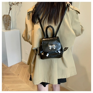 Detail of a black glossy PU leather mini backpack with silver butterfly and pearl accents