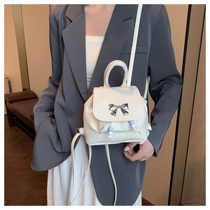 Detail of a creamy white butterfly backpack with metallic bow and colored bead charms
