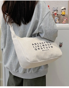 Rear view of model wearing a large cream canvas crossbody bag with letter prints
