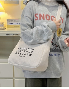 Detail view of cream canvas tote bag with black letter print in a cozy home setting
