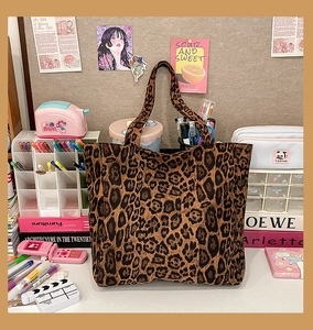 Macro shot of large leopard print tote bag placed on a busy desk with stationery accessories