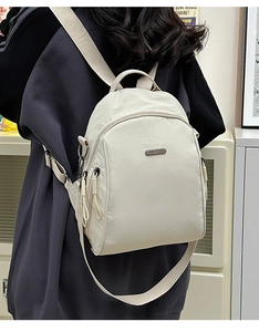 Detailed back view of a beige nylon backpack with wide straps and metal plaque