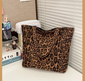 Detail of a large leopard print tote bag placed on a desk with lifestyle accessories