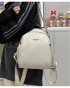 Close-up of cream white nylon backpack with adjustable straps and silver brand plaque