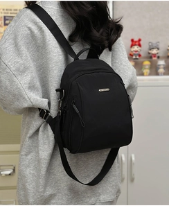 Detail of versatile black nylon backpack showing metal logo plate and adjustable shoulder straps