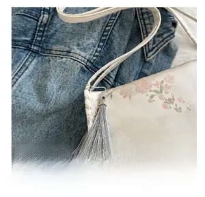 Close-up of elegant floral embroidery and silk tassel on a white satin shoulder bag