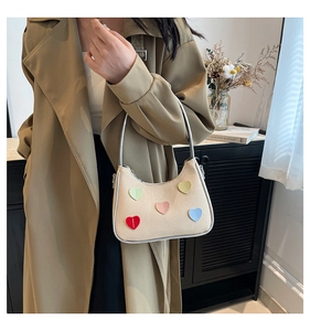 Detail of cream woven handbag featuring colorful heart patches and silver metal handles