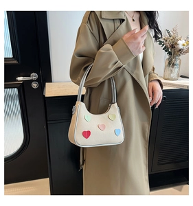 Detail of beige canvas shoulder bag featuring five colorful heart patches and silver trim